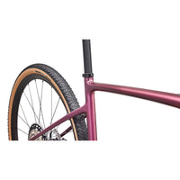 Gravel road bike detail: pink metallic frame and front wheel with knobby tires