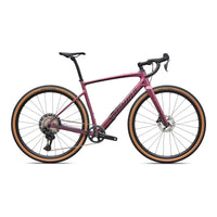 Pink gravel bike with drop handlebars, disc brakes, and tan sidewall tires.