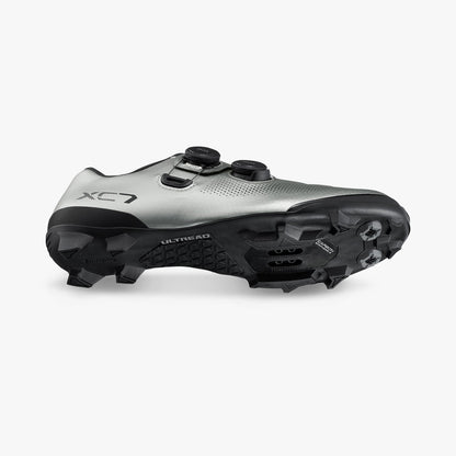 Silver cycling shoe side view showing black traction lugs and cleat hardware